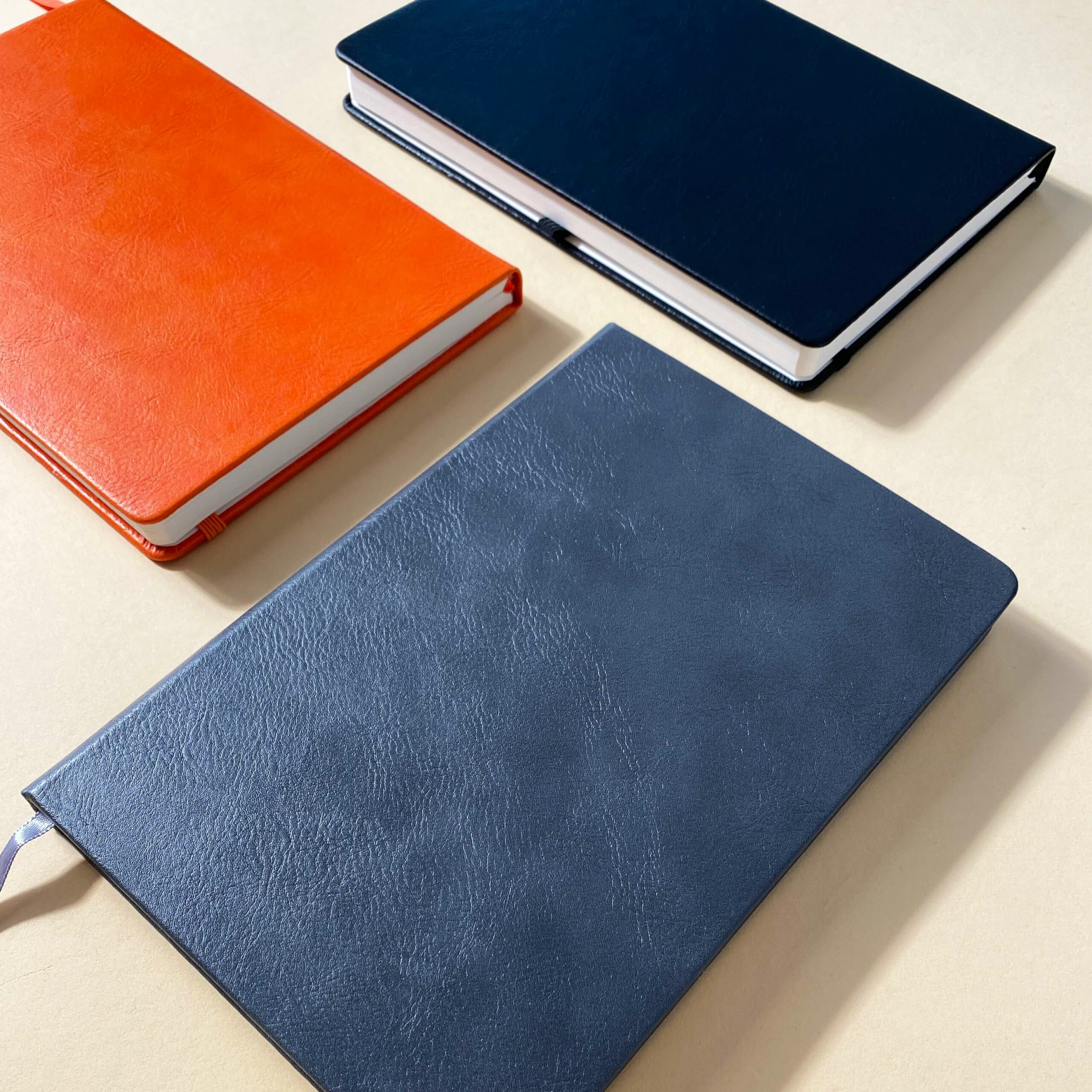Tre anteckningsböcker i blått, orange och mörkblått