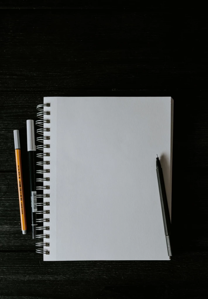 En vit anteckningsbok med tre pennor